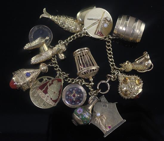 A 18ct gold curb link bracelet hung with assorted gold charms including barrel and articulated fish, gross weight 103.5 grams.
